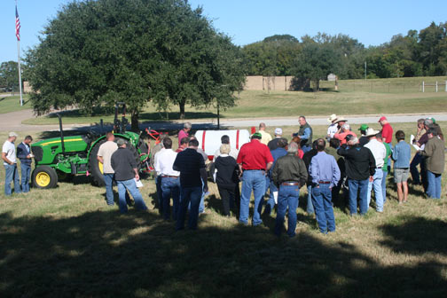 group of people by a tractor with spray rig attached listening to a talk about sprayer calibration